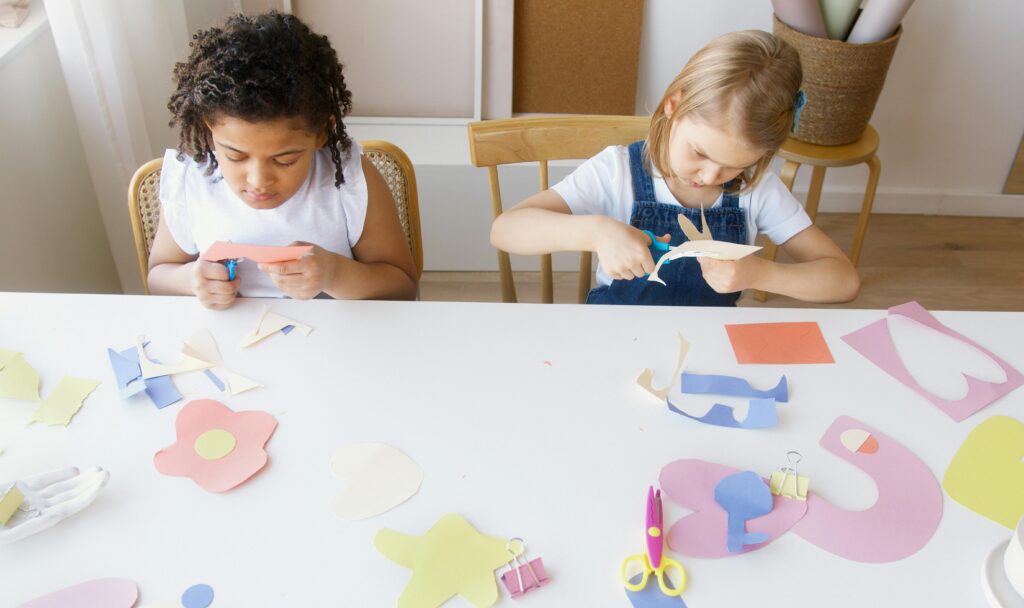 画用紙や折り紙をハサミで切る工作をしている、二人の4歳・5歳くらいの女の子