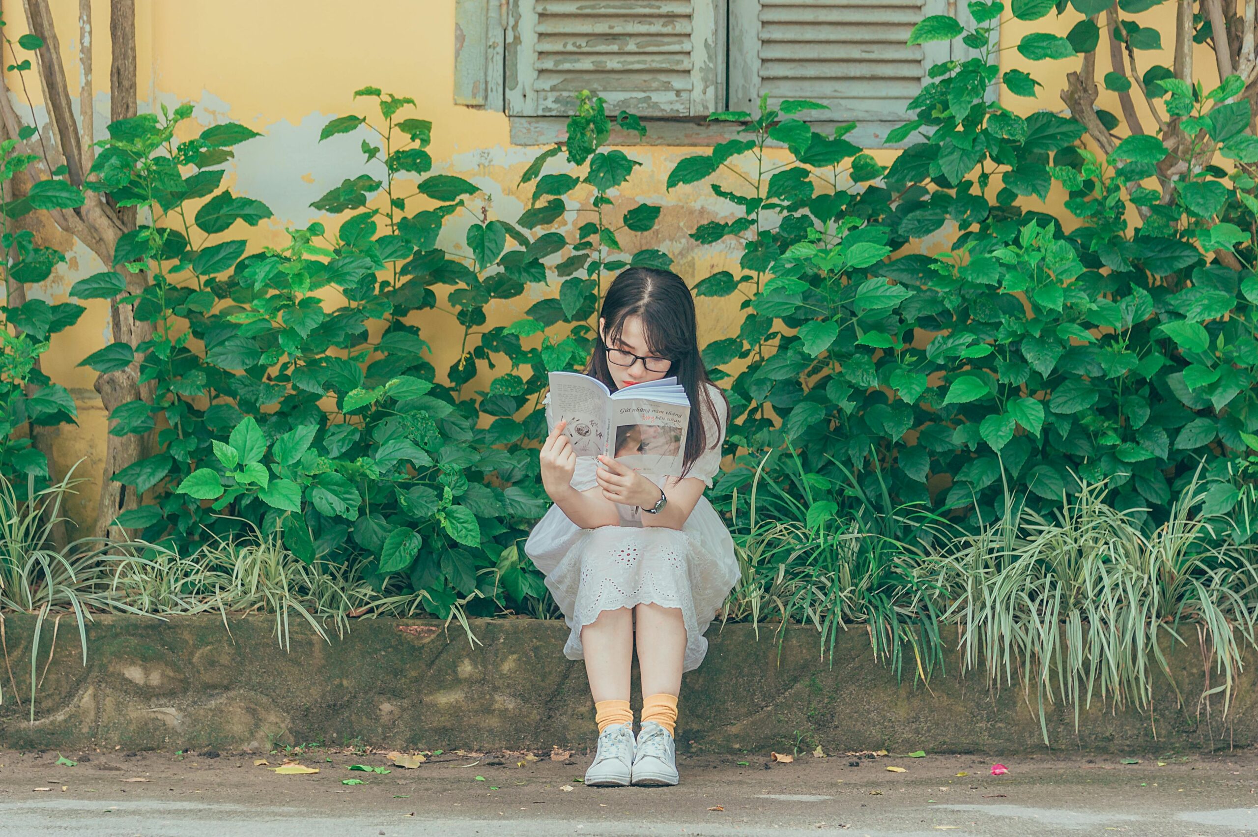 12歳～14歳くらいの女の子が、家の前の道で本を読んでいる写真
