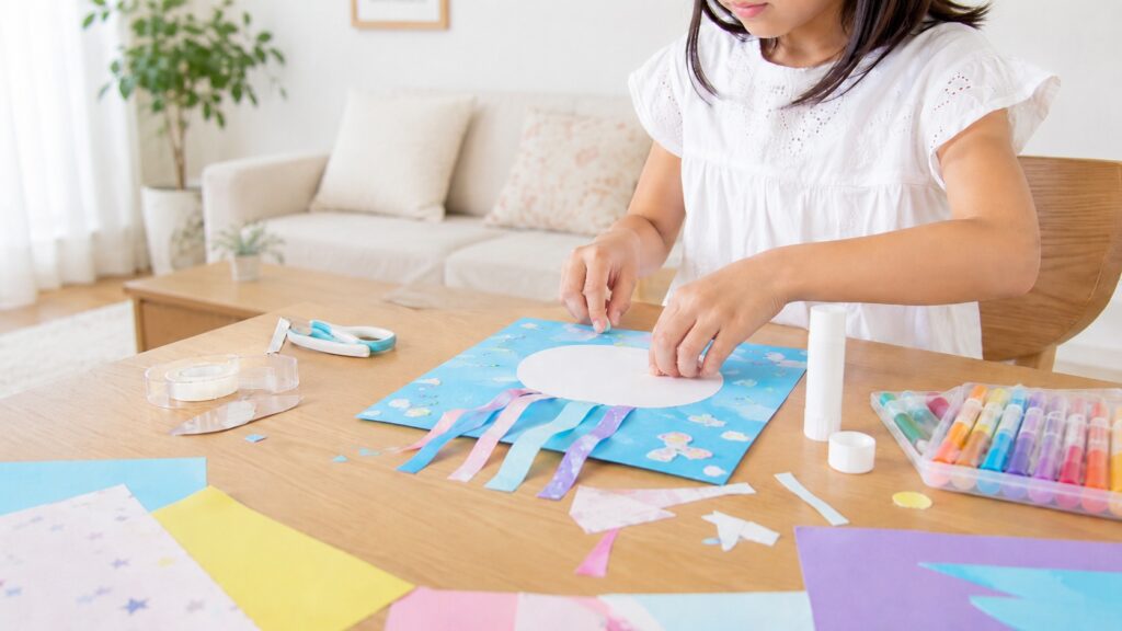 小学生の女の子がリビングのテーブルで色紙やのりを使って工作をしている様子