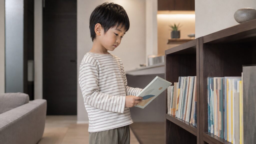 7歳くらいの男の子が自宅の本棚の前で自分に合う読み物を選んでいる様子