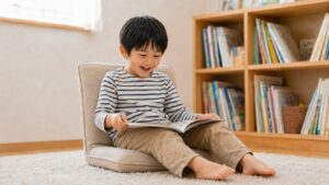 座椅子でくつろぎながら楽しそうに絵本を読む5歳くらいの男の子
