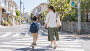 青信号の横断歩道を、手をつないで渡る母親と男の子。日本の住宅街で交通安全を学ぶ親子の様子。